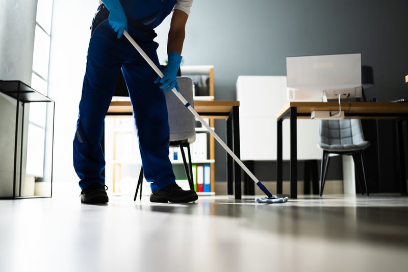 Male Janitor Mopping Floor In Face Mask In Office