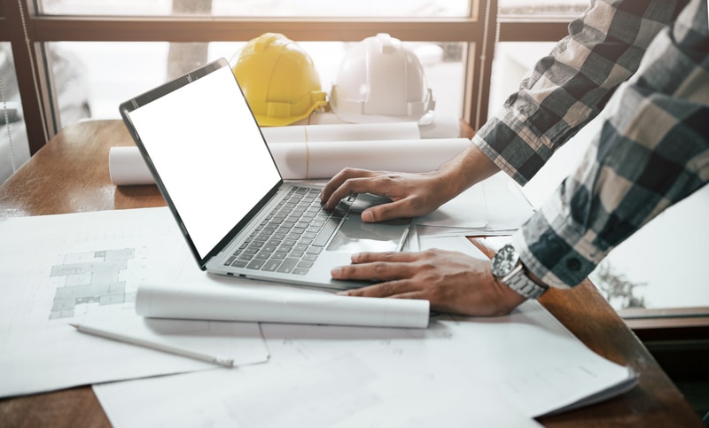 A man conducting facility inspections using a laptop and wearing a hard hat in real-time.