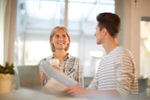 Happy businesswoman with cup of coffee looking at her colleague with paper during discussion of working points