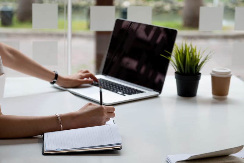 A woman utilizing the Fleet Manager Module for data analysis on her laptop while jotting notes in a notebook at her desk.