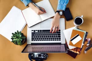 stylish young girl working analytics holding pen on craft background with laptop and papers flat lay