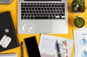 Laptop, cell phone and documents on a yellow desk top view. Business concept