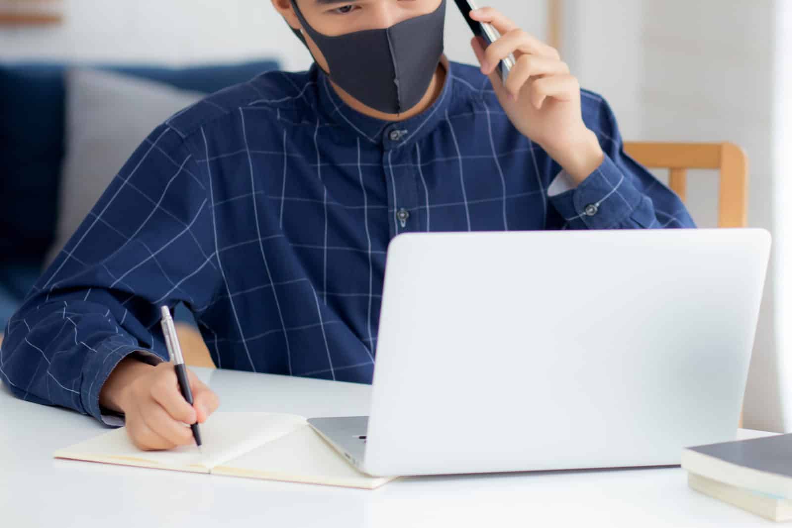 A man utilizing a face mask while effectively working on a laptop, enhancing productivity with module upgrades.