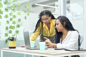 Two young black women reviewing analytical data on various electronic devices. I work in an office for millennial workers.