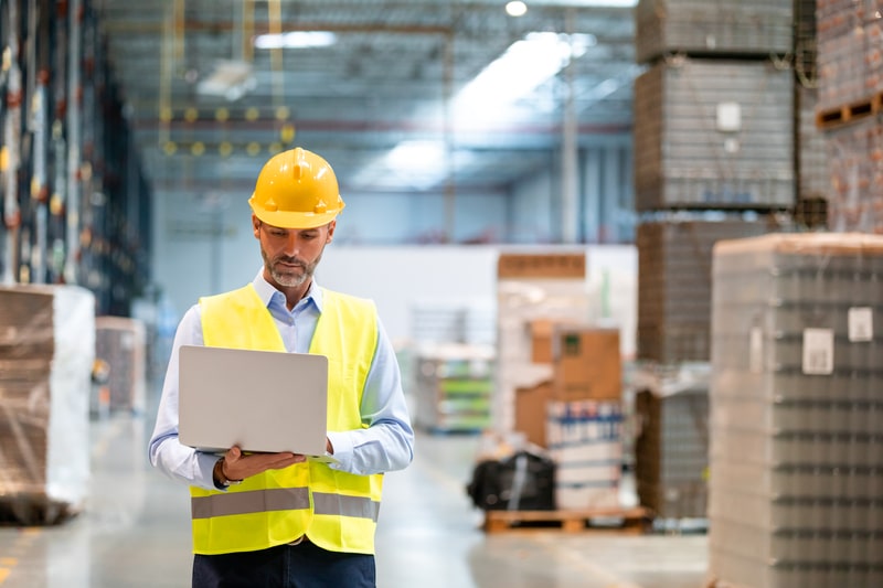 A warehouse worker utilizing a laptop for data analysis in a warehouse.