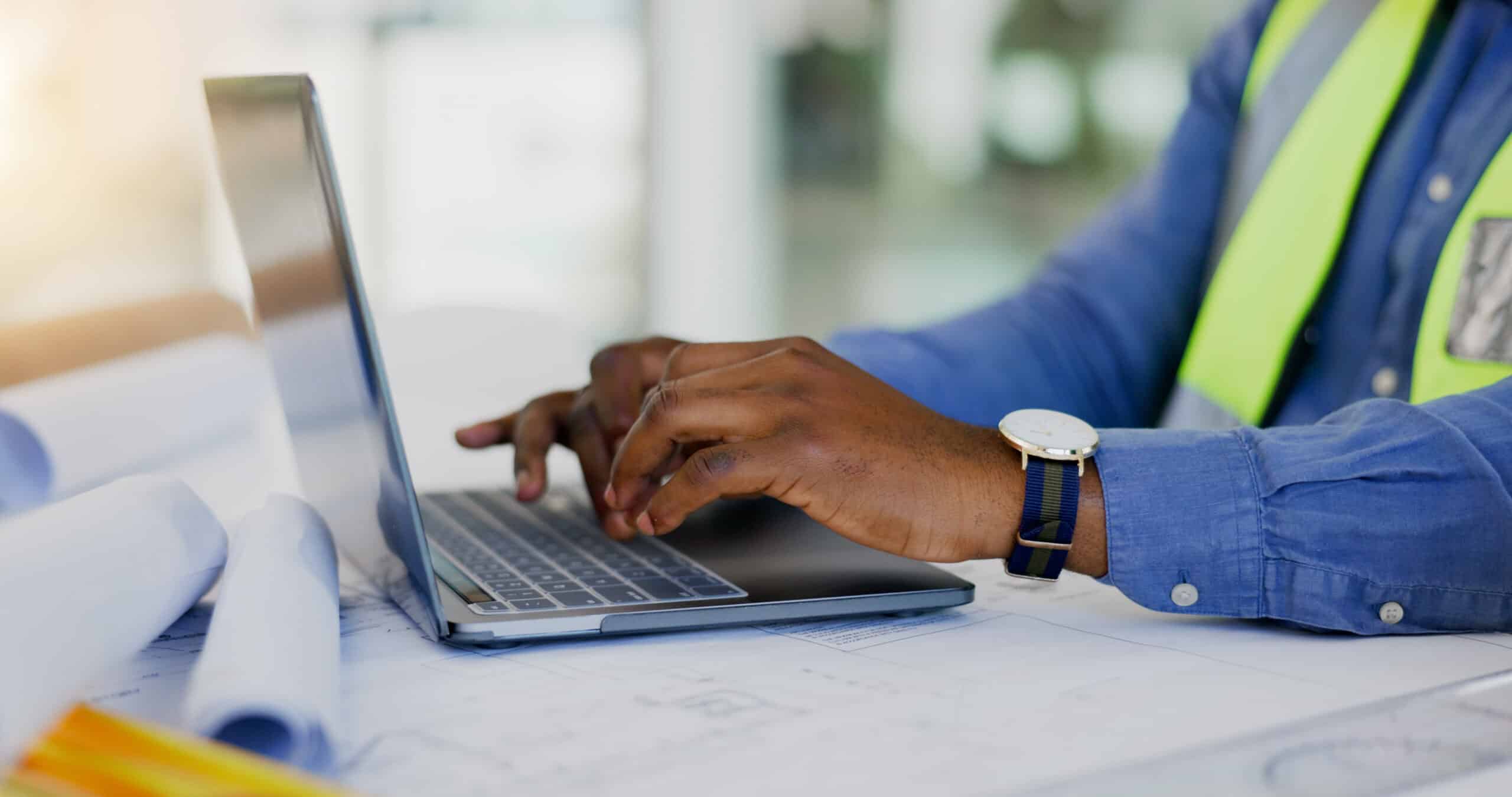 A man enhancing facility management by using a laptop on a desk with blueprints.